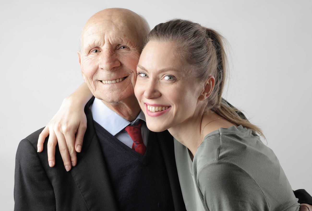 An older man and his adult daughter smiling cheek to cheek