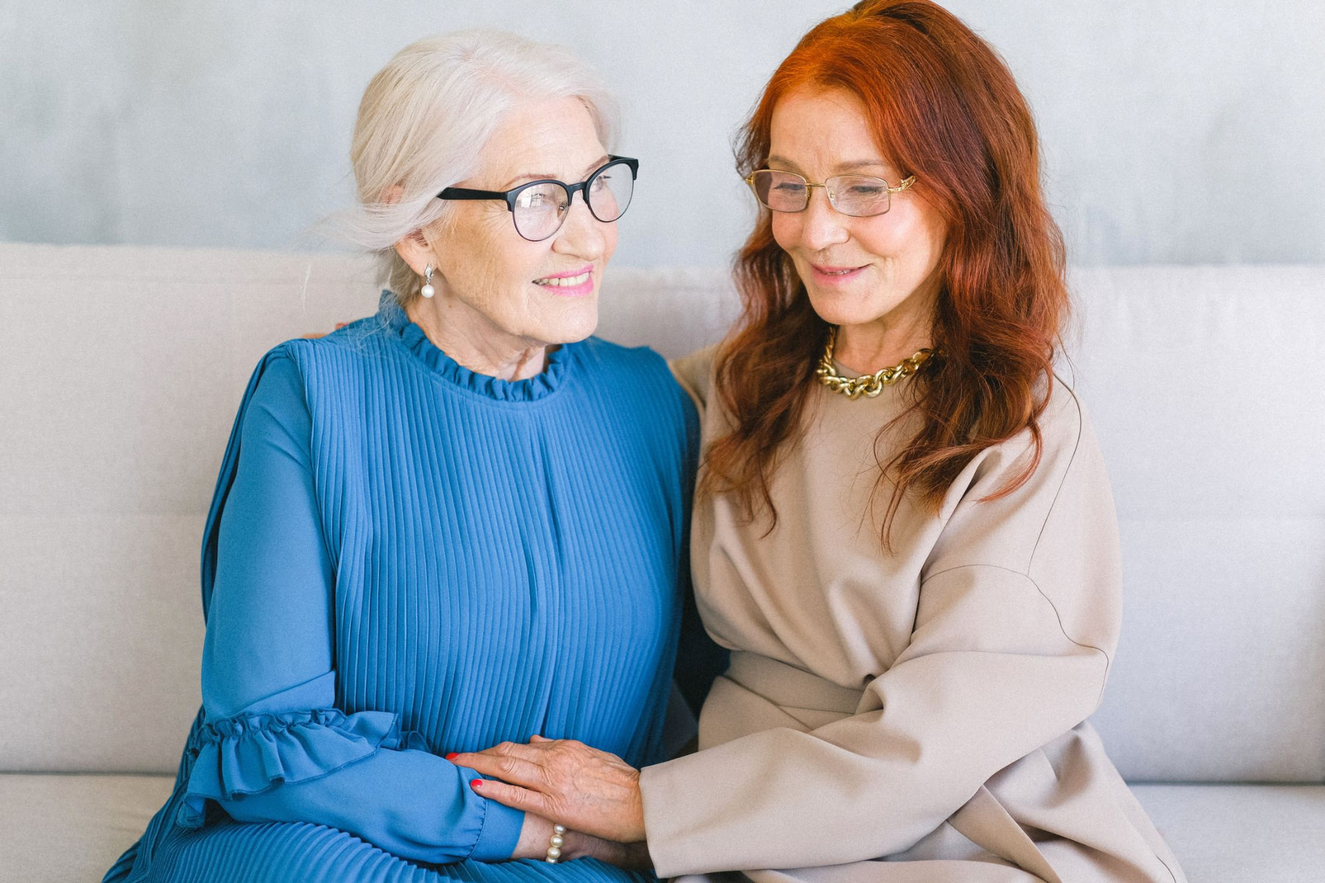 An older woman and her daughter sitting close on a sofa, holding hands